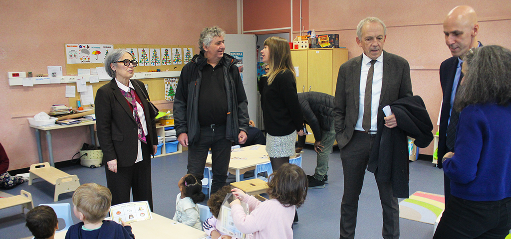 Scolaire : une nouvelle classe pour les tout-petits de petites tables et des enfants de dos au premier plan dans un salle de classe, les adjoints au maire et M. le Maire debout à l'arrière en train de parler