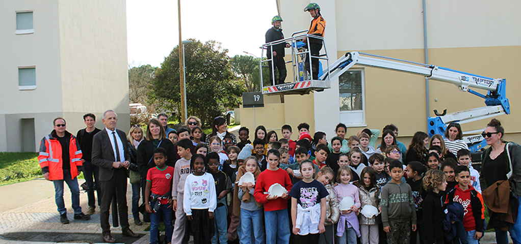 un groupe d'enfants, élus et agents de la ville d'Auch devant des immeubles et une nacelle élévatrice pour l'installation des nids d'hirondelles
